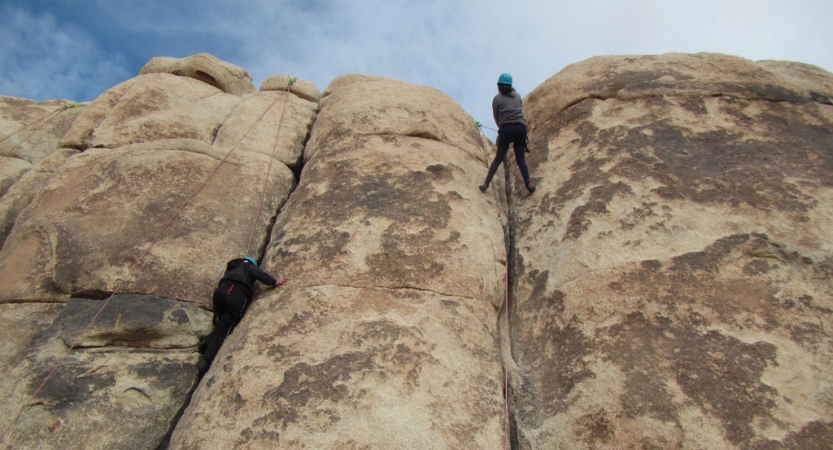 two people wearing safety gear are secured by ropes as they scale a large rock face